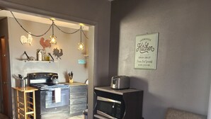 Eine moderne Küche mit Einbauofen, Mikrowelle und Toaster. Ein Holzhocker und ein kleiner Tisch mit Wasserkocher stehen bereit. Die Küche strahlt rustikalen Charme aus, mit Holzboden und einem Schild an der Wand, das "Farmhouse Kitchen" zeigt.