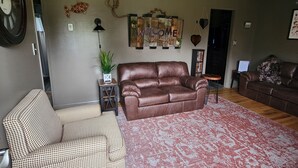 Ein Wohnzimmer mit einem braunen Ledersofa, einem gemusterten Sessel, einem roten und weißen Teppich und einer Wanduhr.