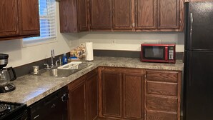 A kitchen with wooden cabinets, a stainless steel sink, a microwave, and a black refrigerator.