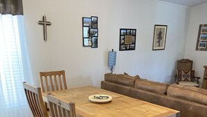 A dining area with a wooden table and chairs, a sofa, and a cross on the wall.