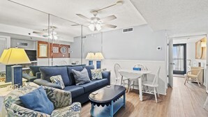 Una sala de estar moderna con un sofá azul, una mesa de centro y un comedor con una mesa y sillas blancas.
