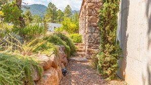 Un chemin de pierres mène à un bâtiment à l’extérieur en pierre, entouré de verdure et d’arbres.