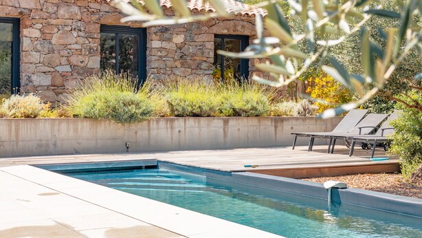 Un bâtiment en pierre avec un toit en tuiles, une piscine et des chaises longues.