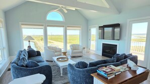 A spacious living room with a high ceiling, large windows, a fireplace, and a television. - Sunrise-Sunset Views From Waterfront Home w/ Elevator (just renovated) (Bethany Beach)
