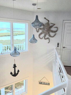 A room with a view of a water body, a white railing, and decorative wall art including an anchor and an octopus.