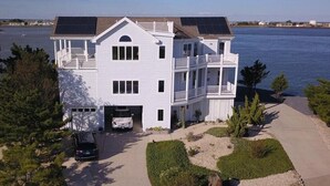 A two-story white building with a garage, a covered porch, and a view of the water. - Sunrise-Sunset Views From Waterfront Home w/ Elevator (just renovated) (Bethany Beach)