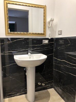 Features a pedestal sink and a gold-framed mirror above.