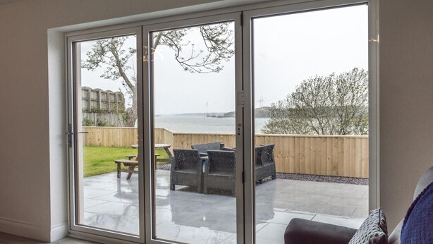 Habitación con puerta de vidrio corrediza que da a un patio exterior con vista al mar y una cerca de madera.