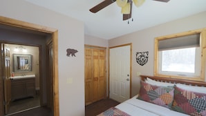 A bedroom with a bed, a wooden ceiling fan, a window with blinds, a door, and a closet. - Willow Cabin (Talkeetna)