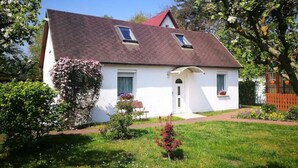 A white house with a brown roof, two skylights, a small front porch, and a well-maintained garden. - Ferienwohnung im Igelbau (Baabe)