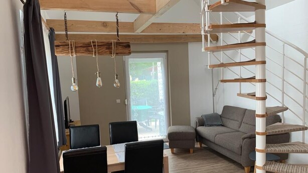 A modern living room with a dining area, a staircase, and a view of the outdoors. - Ferienwohnung im Igelbau (Baabe)
