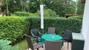 An outdoor patio with a round table and four chairs, surrounded by neatly trimmed hedges. - Ferienwohnung im Igelbau (Baabe)