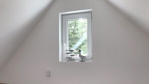 A room with a sloped ceiling, a small window with a view of greenery, and a white door. - Ferienwohnung im Igelbau (Baabe)
