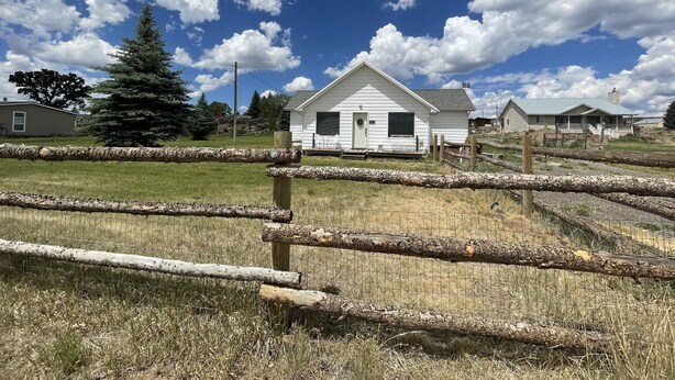 A white house with a front porch, surrounded by a wooden fence and a grassy field. - Callie's Cottage- Cottage stay between Bryce and Zion (Hatch)