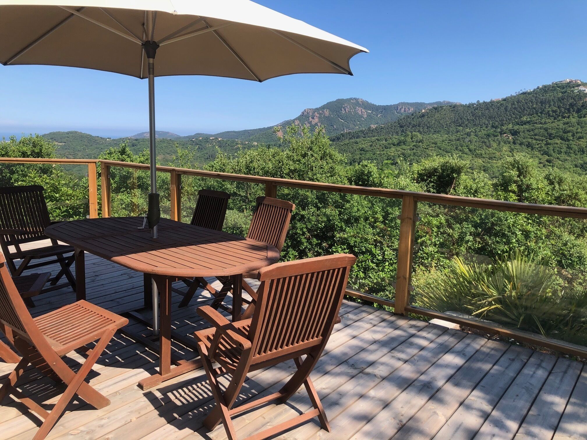 Eine Holzdar Terrasse mit Tisch, Stühlen und Sonnenschirm, mit Blick auf eine gebirgige Landschaft.