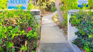 A pathway leading to a beach area with signs indicating beach access and Princess Alexandra National Park.
