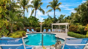 A pool area with lounge chairs, a covered seating area, and lush tropical vegetation.
