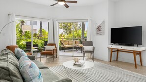 A living room with a sofa, coffee table, TV, and a view of an outdoor patio with furniture.