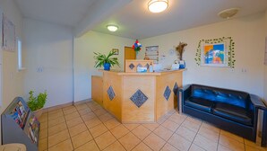 A reception area with a wooden desk, a black leather couch, a potted plant, and a wall calendar. - Budget 8 Motel John Day (John Day)