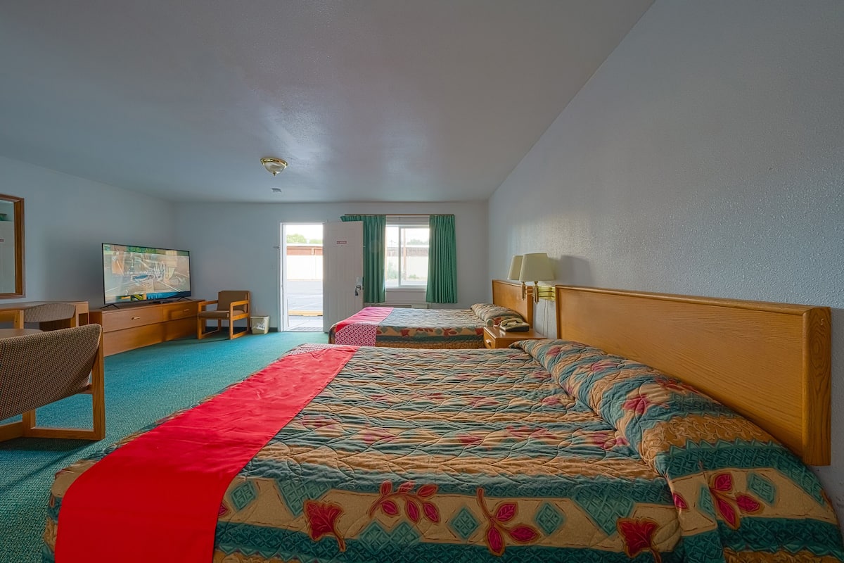 Ein Hotelzimmer mit einem großen Bett, einem Schreibtisch, einem Sessel, einem Fernseher und einem Fenster mit Vorhängen.