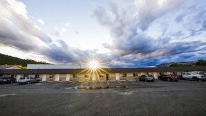 A motel with a parking lot, a building with a flat roof, and a clear sky with clouds. - Budget 8 Motel John Day (John Day)