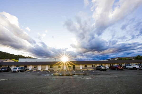 A motel with a parking lot, a building with a flat roof, and a clear sky with clouds.