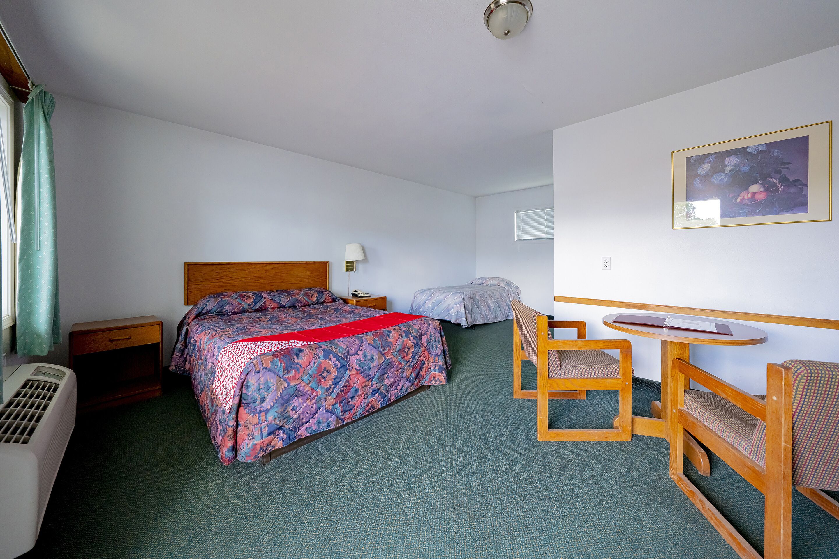 A hotel room with a bed, a desk, a chair, and a small table.