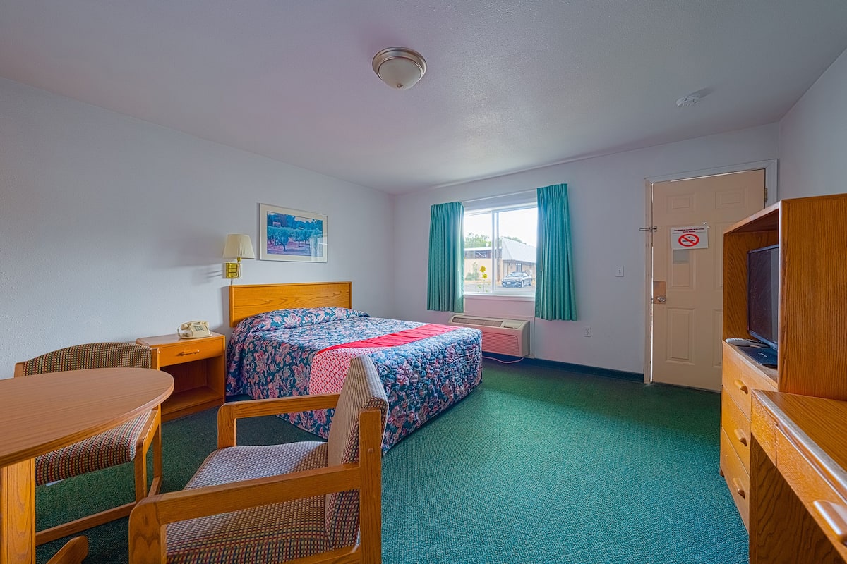 Ein Hotelzimmer mit Bett, Schreibtisch, Stuhl, Fernseher und einem Fenster mit Vorhängen.