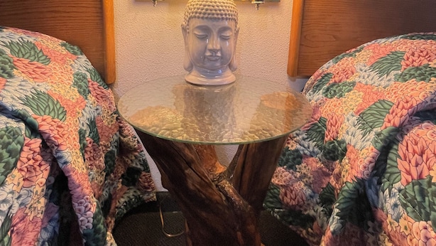 A room with a round glass table, two lamps, a Buddha statue, and floral-patterned bedding. - Budget 8 Motel John Day (John Day)