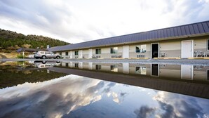 A motel with a row of rooms, a car parked in front, and a body of water reflecting the sky and clouds. - Budget 8 Motel John Day (John Day)