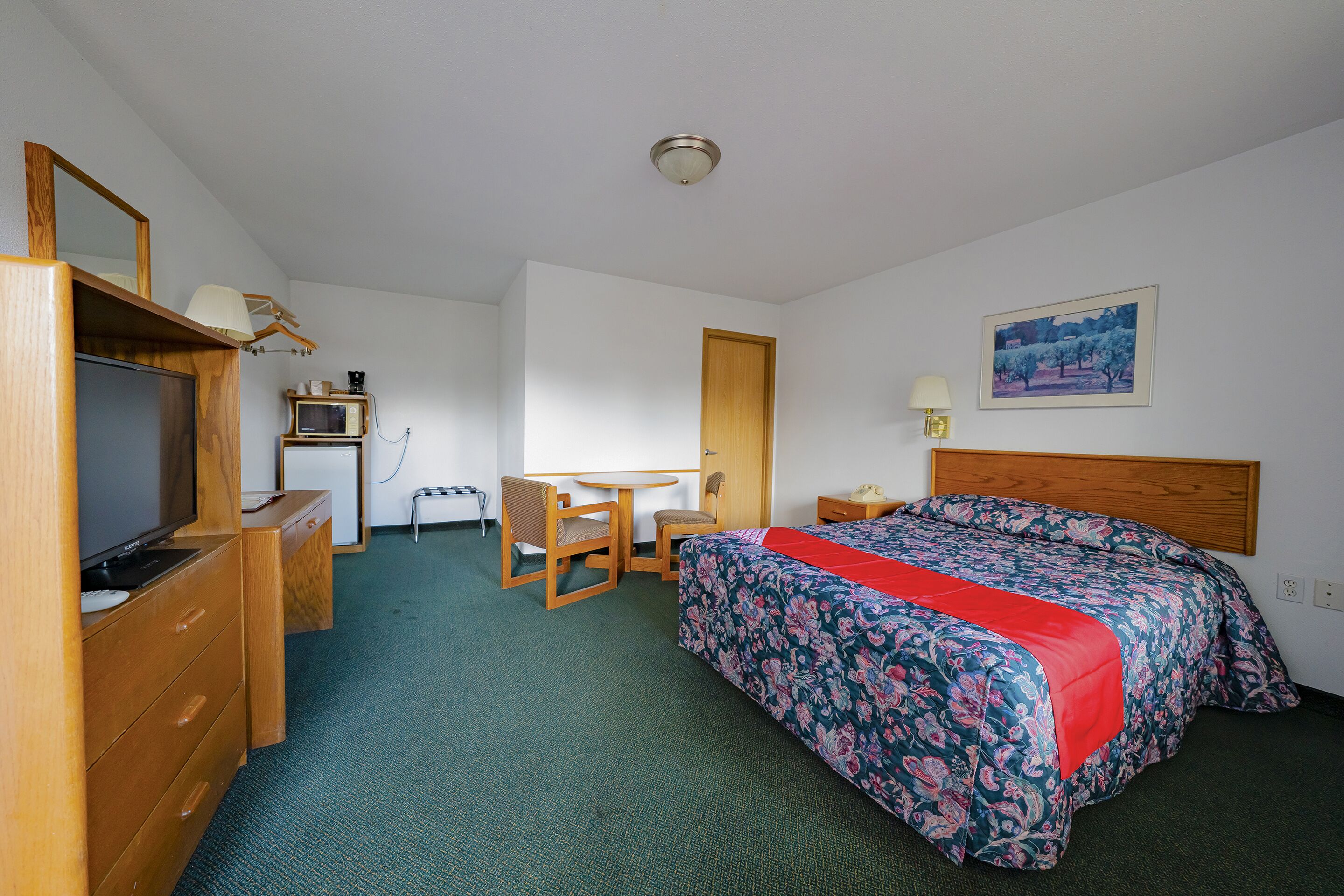 A hotel room with a bed, a desk, a television, and a small table.