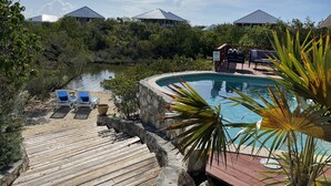 Zona de piscina con muelle de madera, sillas de descanso y vista al río.