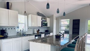 Una cocina moderna con armarios blancos, encimeras de granito y una isla grande con taburetes de bar.