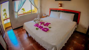 Una habitación de hotel con cama, ventana con cortinas, mesita de noche y lámpara de pared.