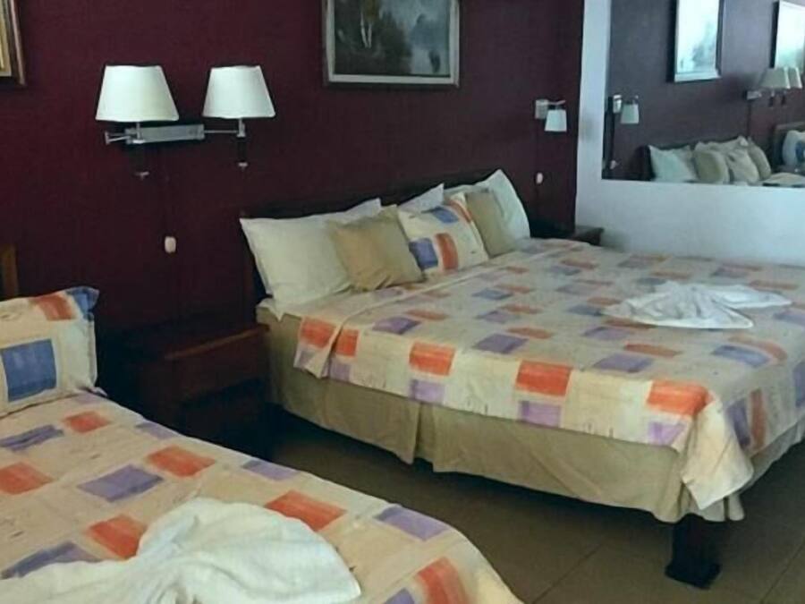Una habitación de hotel con dos camas, cada una con una colcha acolchada y almohadas. Hay lámparas fijadas a la pared y un cuadro enmarcado.