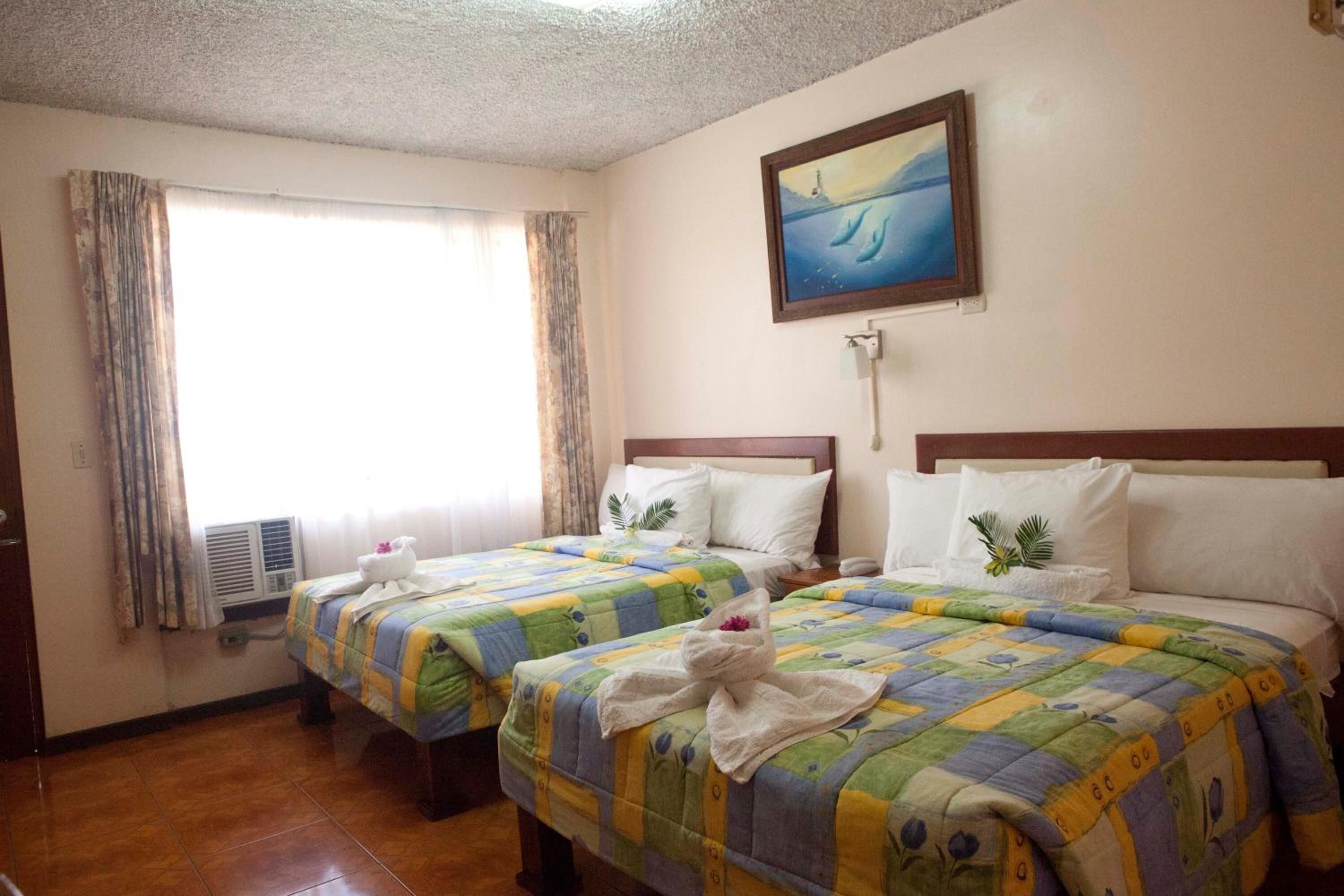 Quarto de hotel com duas camas, um quadro na parede e uma janela com cortinas.