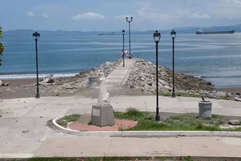 A coastal walkway with stone steps leading to the beach, surrounded by lamp posts and a clear view of the sea.