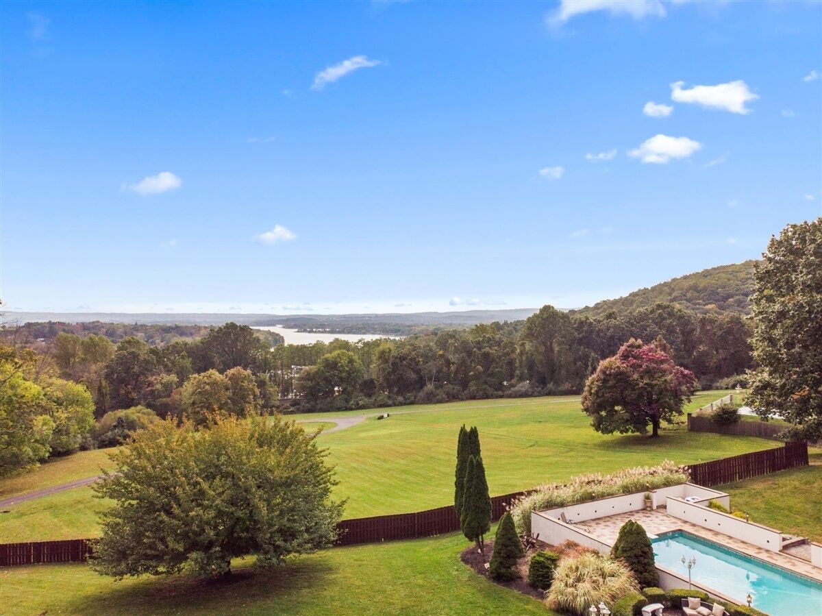 A backyard with a swimming pool, a fenced area, and a view of a lake and hills.