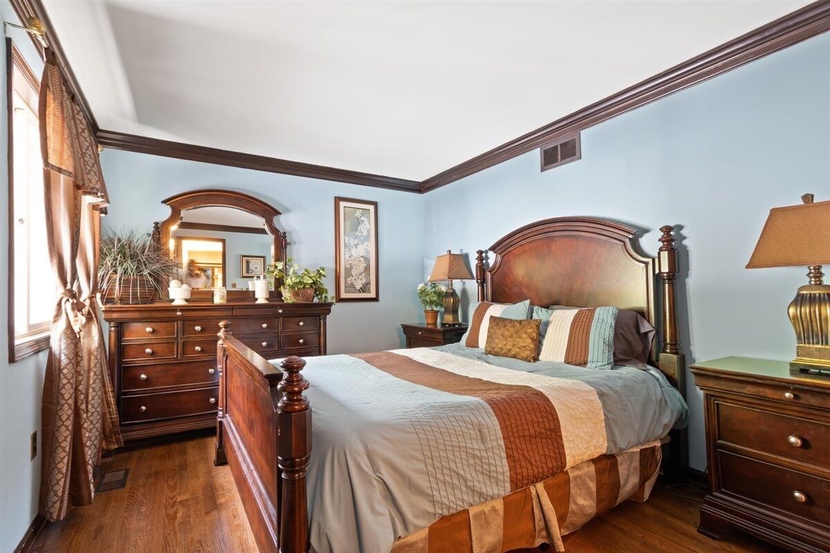 A bedroom with a wooden bed, a dresser, a nightstand, and a mirror.