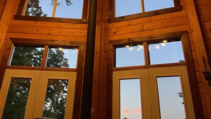 A wooden interior with a chandelier, large windows, and a high ceiling.