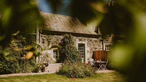 Une maison en pierre avec un jardin, une porte en bois et une petite table entourée de chaises.