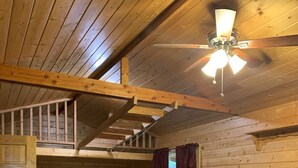 A cozy cabin interior with a wooden ceiling, a ceiling fan, a kitchenette, a plaid-patterned bed, and a wooden chair. - The Bear Cabin a rustic ranch cabin (Freedom)