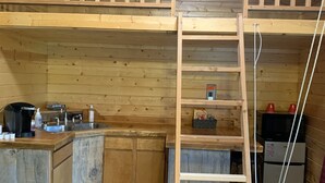 A compact kitchen with wooden cabinets, a sink, and a microwave. A wooden ladder is positioned against the wall. - The Bear Cabin a rustic ranch cabin (Freedom)