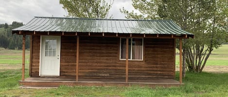 A small wooden cabin with a metal roof, a white door, and a window.