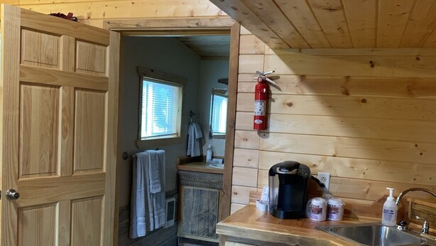 A wooden cabin interior with a kitchen area, including a coffee maker, sink, and a fire extinguisher. - The Bear Cabin a rustic ranch cabin (Freedom)