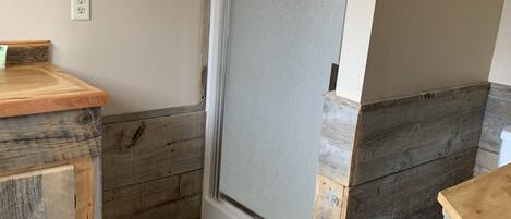 Un baño con ducha, suelo de madera, un lavabo con encimera de madera y un perchero para toallas.