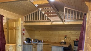 A cozy cabin interior with a wooden ceiling, a small kitchenette, a sofa, and a wooden door. - The Bear Cabin a rustic ranch cabin (Freedom)