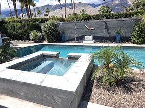 Piscina con cubierta de piedra, plantas de palma y vista a las montañas.