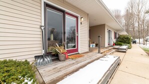 A single-story house with a front porch, a red door, and a small garden area with a potted plant and a metal bench. - Awesome in Walloon Village (Walloon Lake)