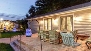 A patio with wicker furniture and glass vases, a covered area with a table and chairs, and a house with a covered porch.